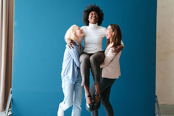 istock Diverse Friends Laughing Together While Lifting Young Woman Against Blue Studio Background 2221779961