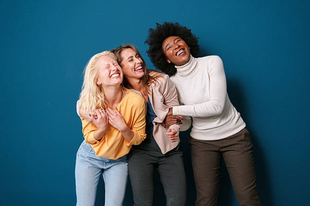 istock Three Diverse Women Laughing and Embracing Against a Blue Backdrop 2221779969