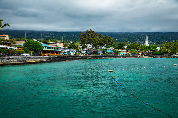 Kailua-Kona town directly on the ocean, view of the shops, restaurants and other businesses along Alii Drive, mostly cloudy sky, west coast of the Big Island of Hawaii.  Photo taken on October 2, 2024.