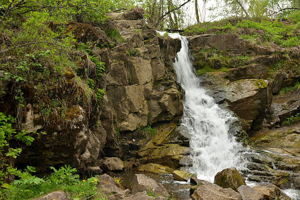 istock A small waterfall flows in a rapid cascade from a stone wall surrounded by forest on a cloudy summer day. 2221782484
