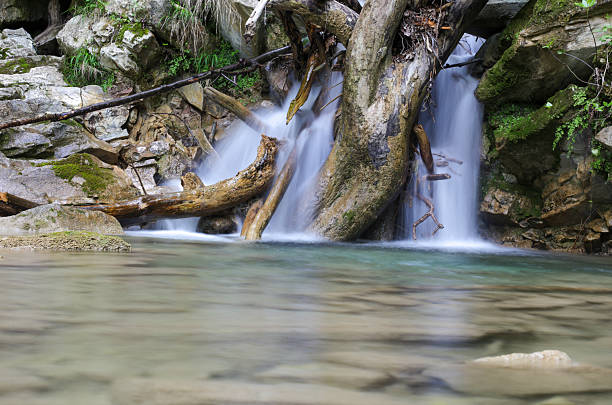 A stream of water flows down a rocky hillside. The water is clear and calm, and the rocks are scattered throughout the scene. Scene is peaceful and serene, as the water flows gently over the rocks