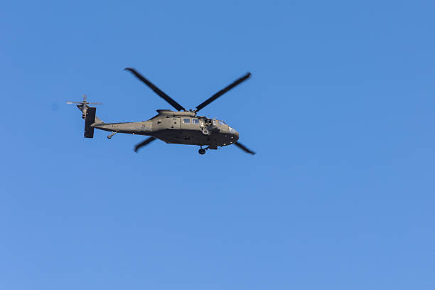 A U.S. Army UH-60 Black Hawk helicopter captured mid-flight against a vivid blue sky, showcasing its powerful rotor blades and tactical design. The image emphasizes military aviation, defense readiness, and modern airborne technology. Suitable for editorial or illustrative use in topics related to national security, aerospace engineering, military operations, or government infrastructure.