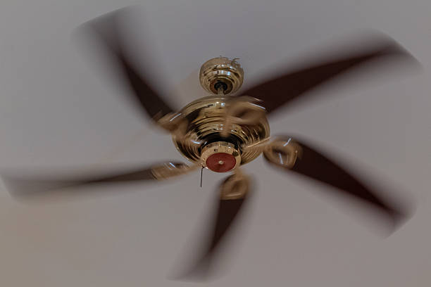 istock Classic brass ceiling fan with dark wooden blades spinning rapidly overhead 2221808421