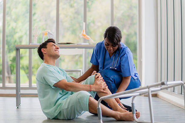 istock Male patient falling down with knee pain during a physical therapy session, with a nurse rushing to help. Accident or injury concept, a man suffering from leg pain in a hospital rehabilitation center. 2221808997