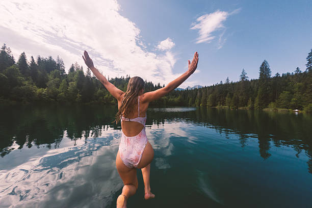 istock Woman Leaping into Tranquil Lake Surrounded by Forest 2221813231