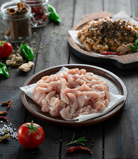 Fresh raw chicken breast cut into small finger pieces, dark surface.