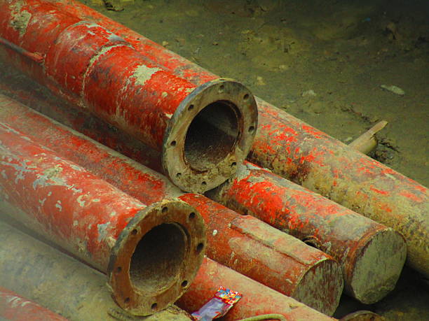istock Stack of red metal pipes arranged on a sandy surface 2221824838