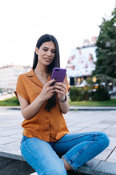 istock Young woman using smartphone while sitting outdoors in urban setting 2221825393