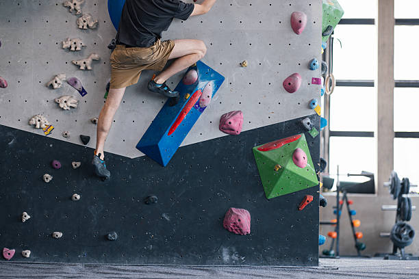 A climber scaling an indoor bouldering wall with colorful holds inside a climbing gym. The image captures the athleticism and determination involved in the climbing activity.