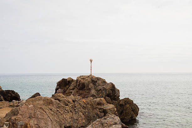istock Solitary white pole on rocky seashore against overcast sky 2221829598