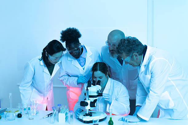 Multi-ethnic team of scientists analyzing sample under microscope in modern laboratory
