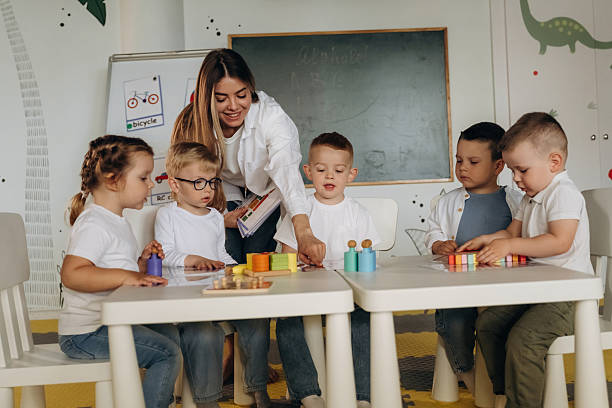 istock Smiling, learning, playing game by table. Children in kindergarten with their teacher 2221831075