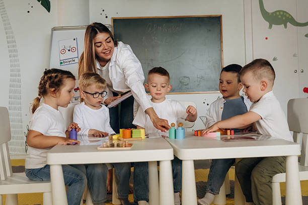 istock Smiling, learning, playing game by table. Children in kindergarten with their teacher 2221831082