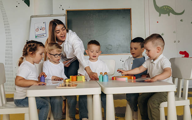 istock Smiling, learning, playing game by table. Children in kindergarten with their teacher 2221831087