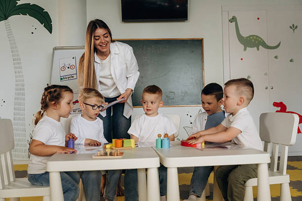 istock Smiling, learning, playing game by table. Children in kindergarten with their teacher 2221831138