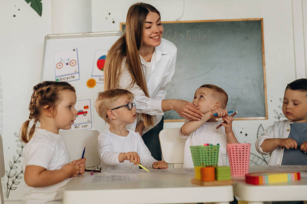 istock Drawing by the table. Children in kindergarten with their teacher 2221831183