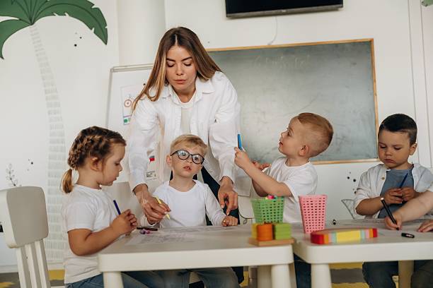 istock Drawing by the table. Children in kindergarten with their teacher 2221831200