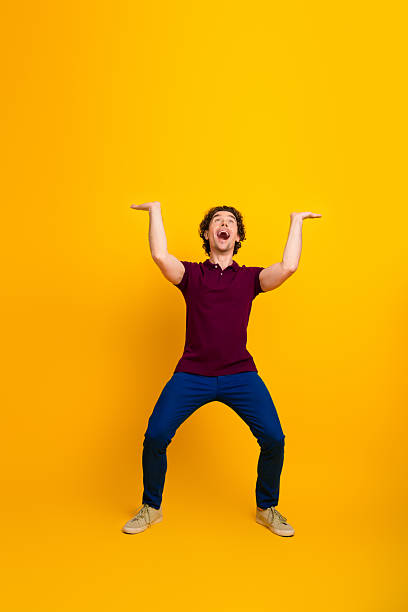 istock Young man in trendy casual attire expressing joy while gesturing with hands against a vibrant yellow background 2221832056
