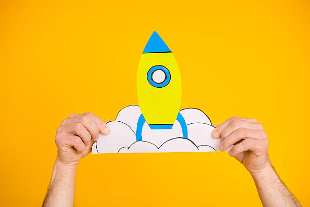 istock Bright yellow background showcasing hands holding a craft paper rocket with clouds representing creativity and imagination 2221832067