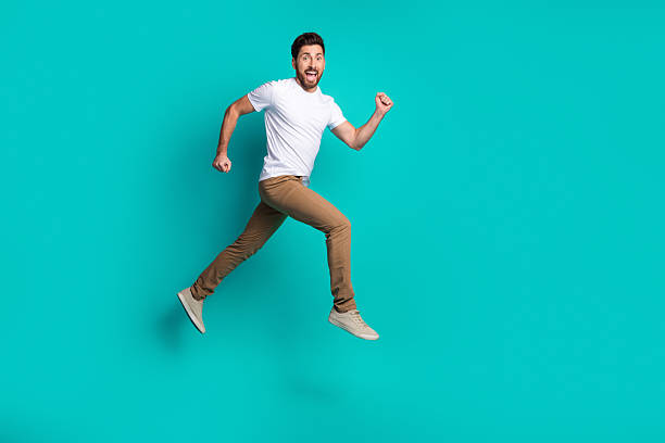 istock Energetic man jumping in casual style with cheerful expression on a vibrant teal background, showcasing dynamic emotions 2221832412