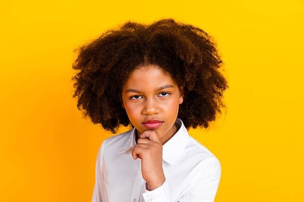 istock Confident schoolgirl posing with thoughtful expression against a vibrant yellow background, wearing a white formal shirt 2221832995