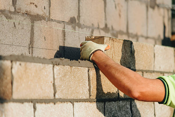 istock Close-up of Bricklayer constructing stone wall using stone blocks, cement mortar mix and trowel while wearing gloves 2221840754