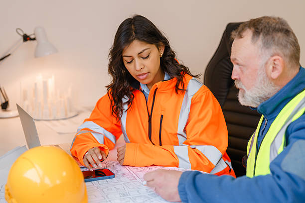 istock Female structural engineer collaborating with male project manager on construction plans in office with safety gear and technology around 2221841432