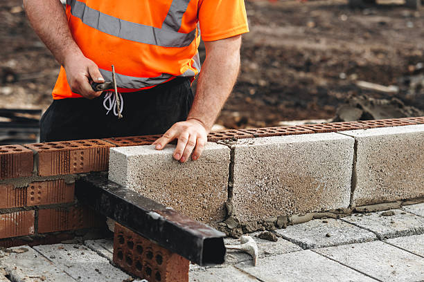 istock Skilled bricklayer working on construction site laying concrete footing blocks for wall construction 2221842195
