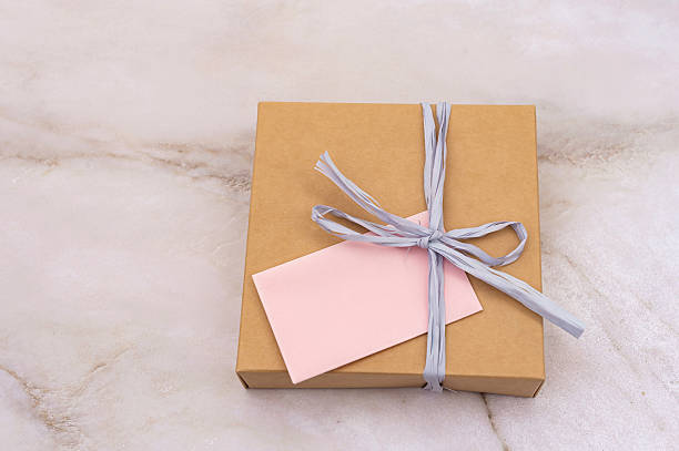 istock National Cartonnage Day. Wrapped Gift Box with Pink Note on Marble Background 2221842360