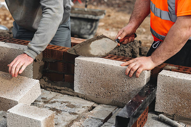 istock Skilled bricklayer working on construction site laying concrete footing blocks for wall construction 2221842402
