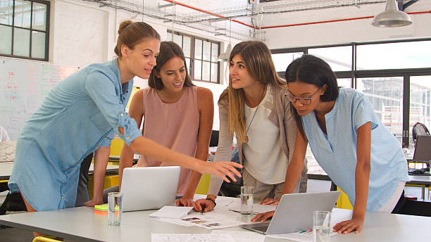 istock Four Young Businesswomen Standing Around Table With Laptops And Documents 2221842767