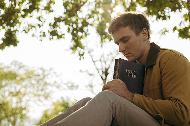 istock Young man praying outdoors with Bible in arms 2221843977
