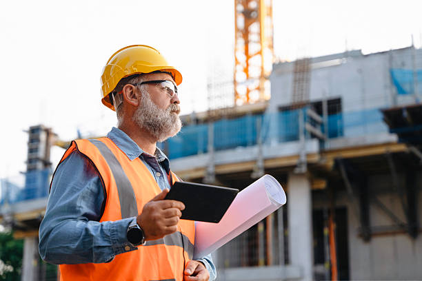 istock A construction supervisor in a safety vest and hard hat is observing the site, holding plans while overseeing building activity amidst cranes and construction workers in an urban area 2221851140