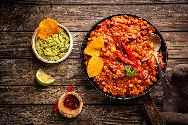 Mexican hot chili con carne in a pan with tortilla chips on dark background, top view