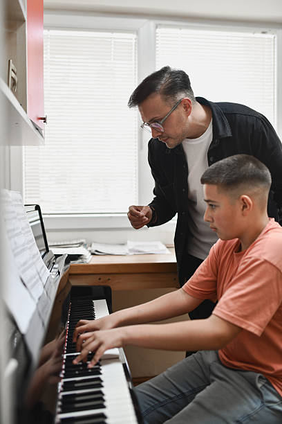 istock Male Instructor Standing Supportively Beside Student During Focused Piano Practice Session 2221863605