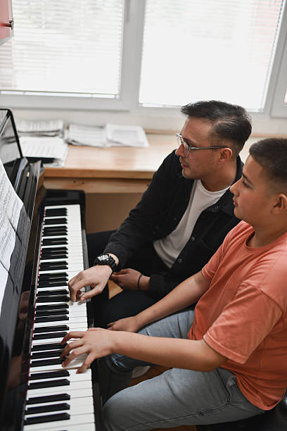 istock Male Piano Instructor and Young Student Performing Piece Together With Careful Coordination 2221863640