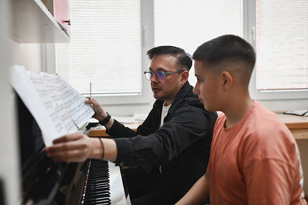 istock Focused Teacher Pointing at Sheet Music While Guiding Young Pianist During Lesson 2221863748
