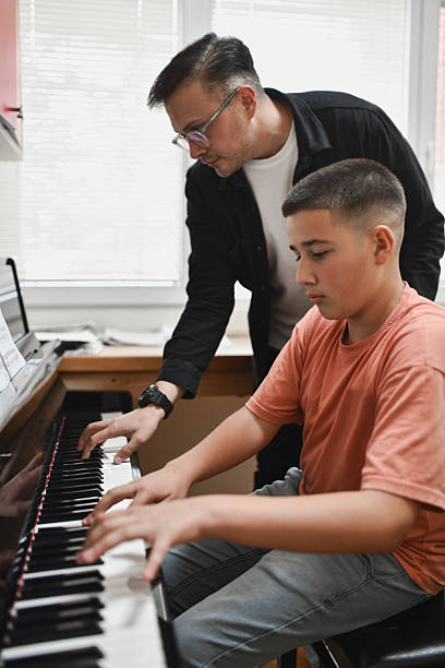 istock Experienced Pianist Playing Alongside Young Student While Practicing Sheet Music Together 2221863960