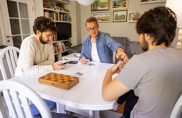 istock Two generations playing cards at home , chess on the table 2221866828