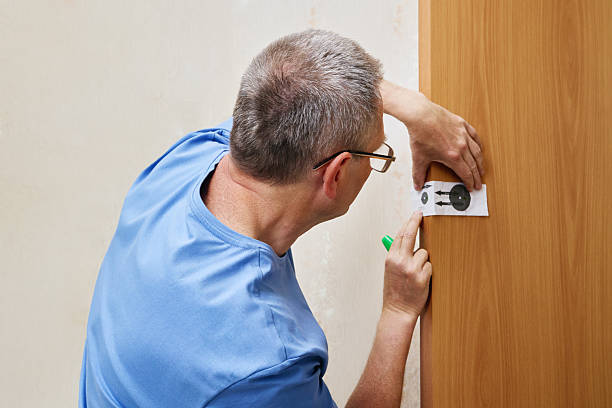 istock Preparing surface for latch placement man aligns paper template with door edge and carefully marks drilling spots using reference arrows on guide. 2221872073