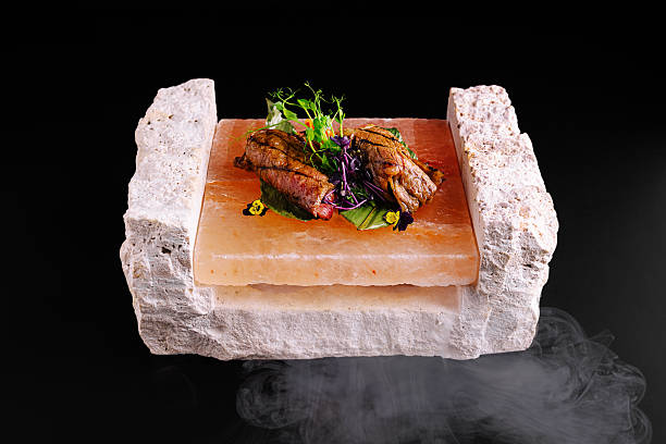 Tender beef steak rests on a solid salt block, garnished with fresh herbs and colorful edible flowers. The dish is presented against a black background, creating an elegant atmosphere.