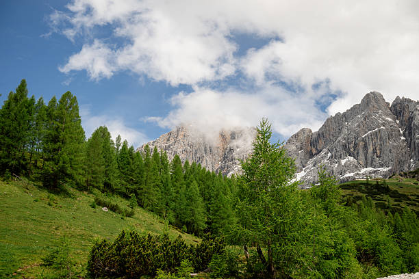 Dramatic Dachstein mountain peaks with lush green valley and clouds in Austria
