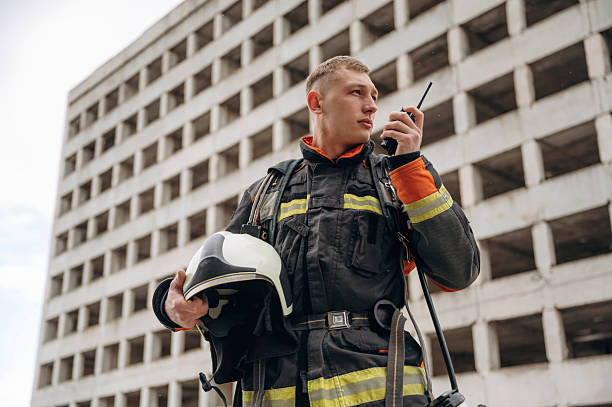 istock Conversation by walkie talkie. Professional firefighter is standing outdoors against big unfinished building 2221874265