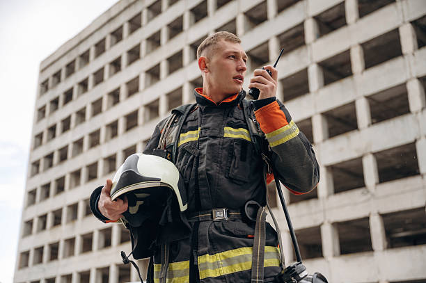 istock Conversation by walkie talkie. Professional firefighter is standing outdoors against big unfinished building 2221874269