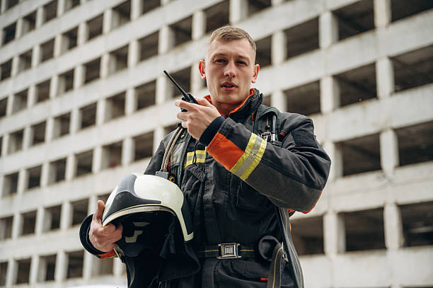 istock Conversation by walkie talkie. Professional firefighter is standing outdoors against big unfinished building 2221874277