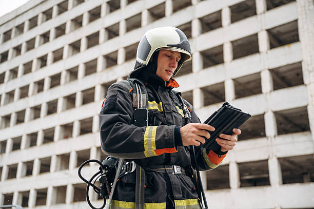 istock Tablet in hands. Professional firefighter is standing outdoors against big unfinished building 2221874334