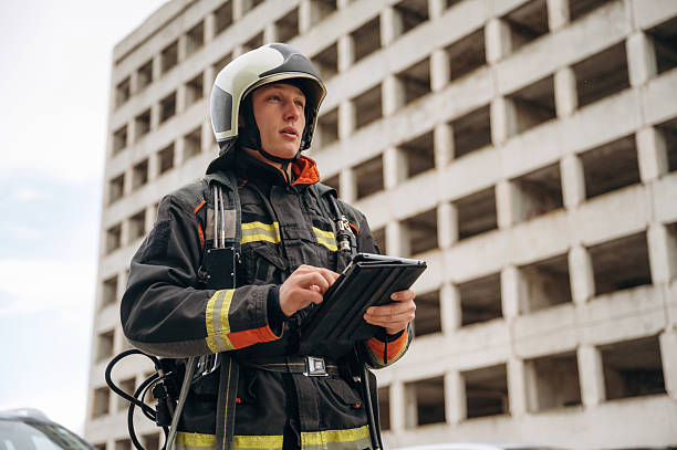 istock Black notepad is in hands. Professional firefighter is standing outdoors against big unfinished building 2221874353