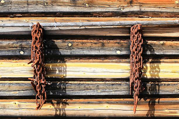 Rusted chains hang from a wooden cabin wall, casting long shadows in the morning light.