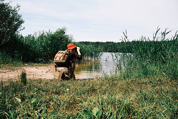 Forest lake in summer. Female hiker is watching birds using binoculars