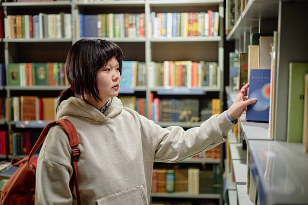istock Young Adult Asian Woman Selecting Book from Library Shelf While Studying 2221879254